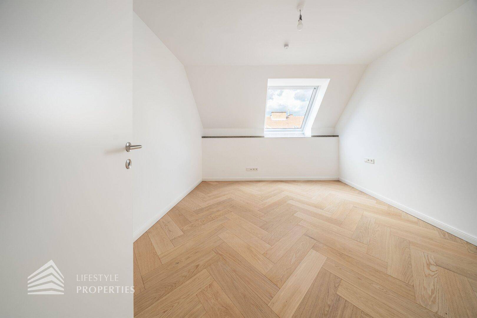 Ruhiges Schlafzimmer im Dachgeschoss mit hellem Parkettboden und einem Dachfenster.