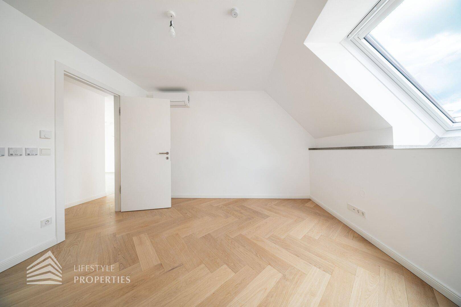 Geräumiges Schlafzimmer im Dachgeschoss mit hellem Fischgrätparkett und Dachfenster.