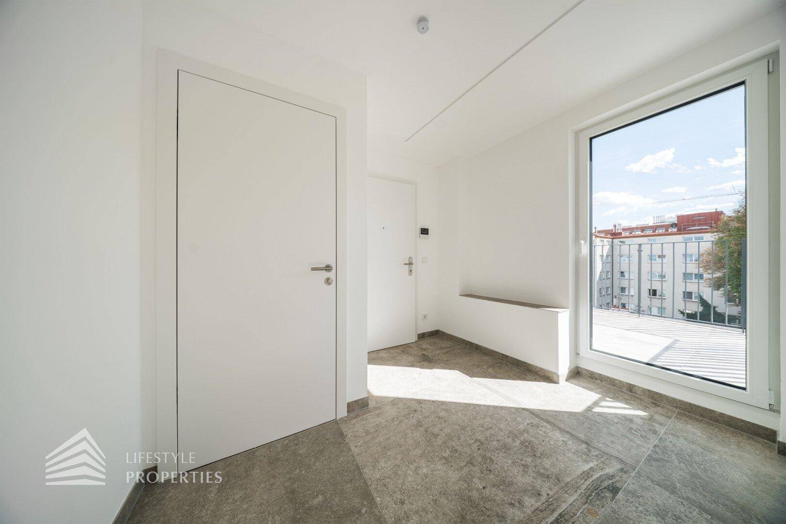 Heller Eingangsbereich mit grauen Fliesen und großem Fenster mit Zugang zum Außenbereich.