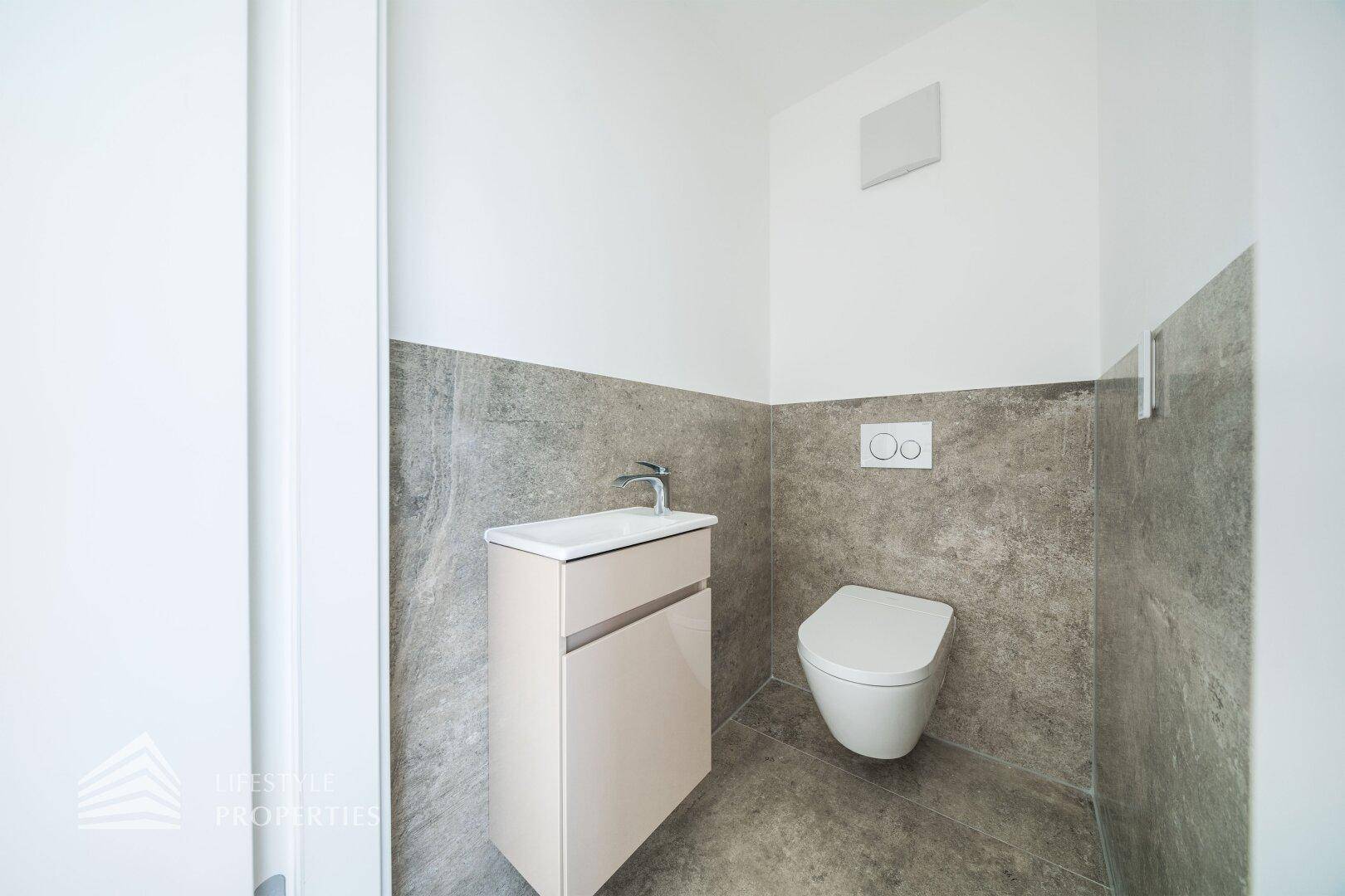 Modernes Gäste-WC mit grauen Fliesen, wandhängendem WC und kleinem Waschbecken.