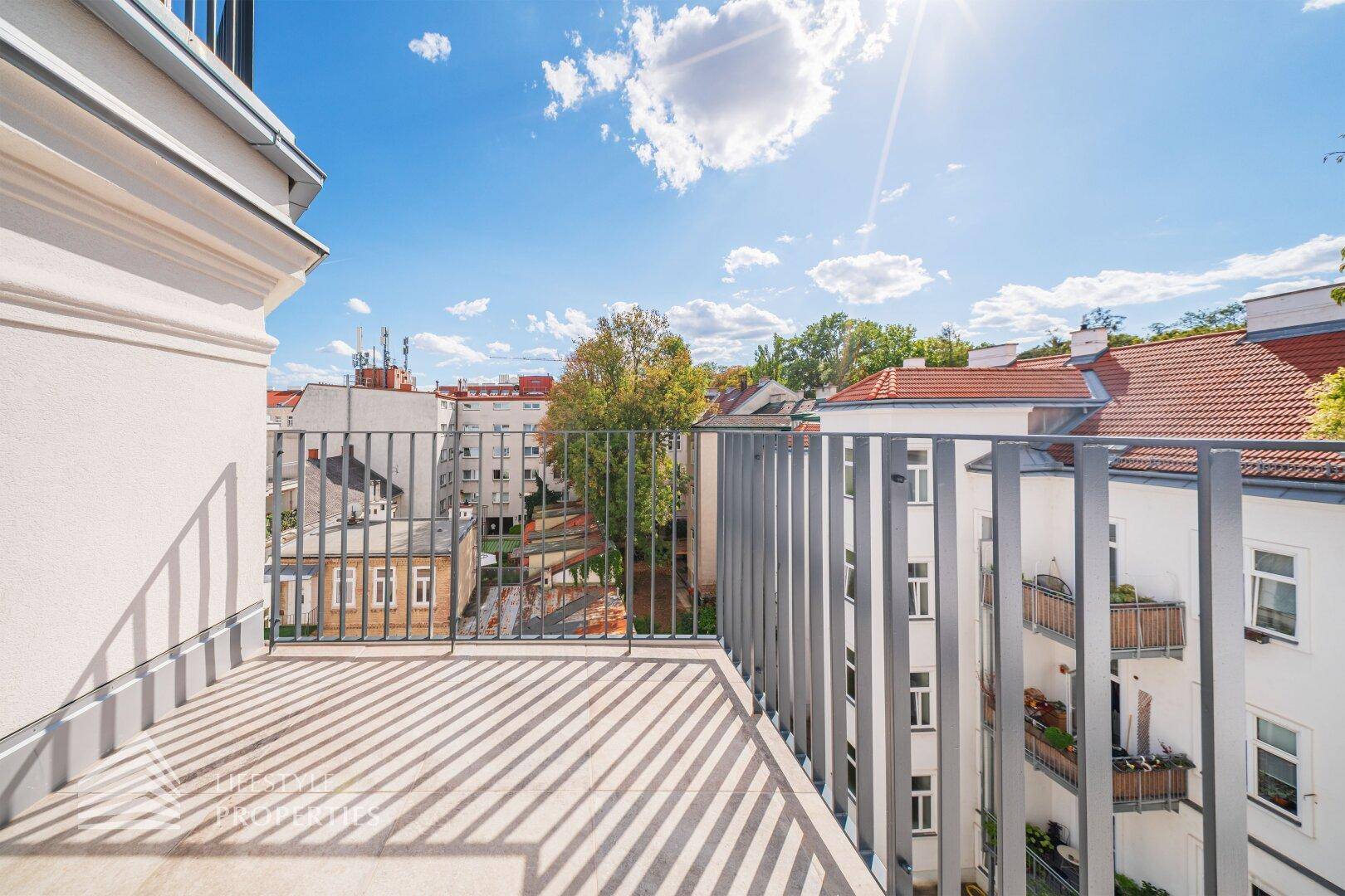 Sonniger Balkon mit Blick auf die umliegenden Gebäude und viel Grün.