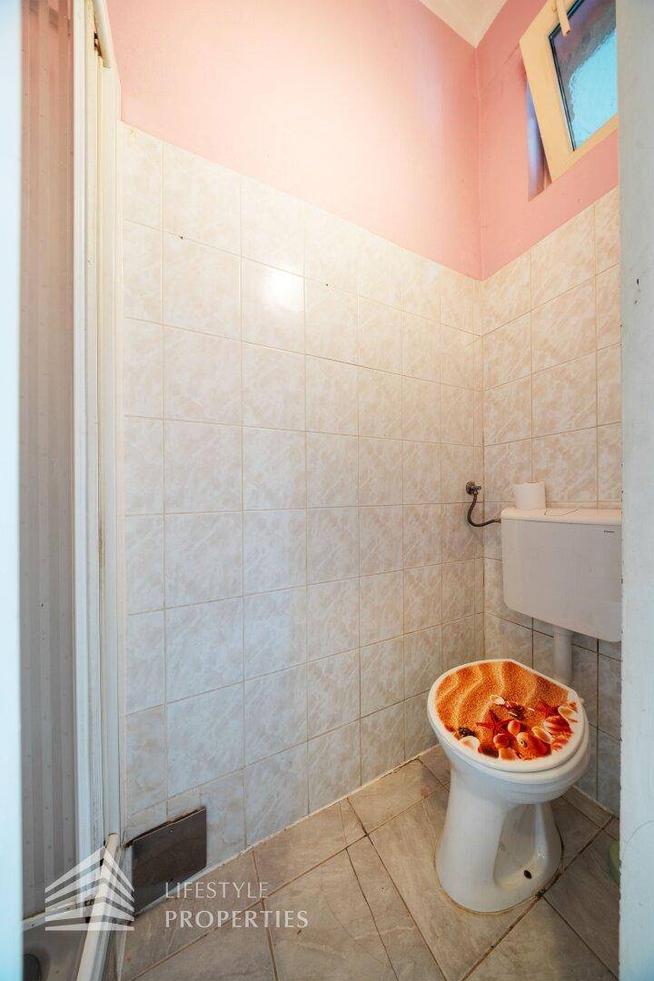 Kleines WC mit rosa Wänden, weißen Fliesen und einer Toilette mit gemustertem Sitz.