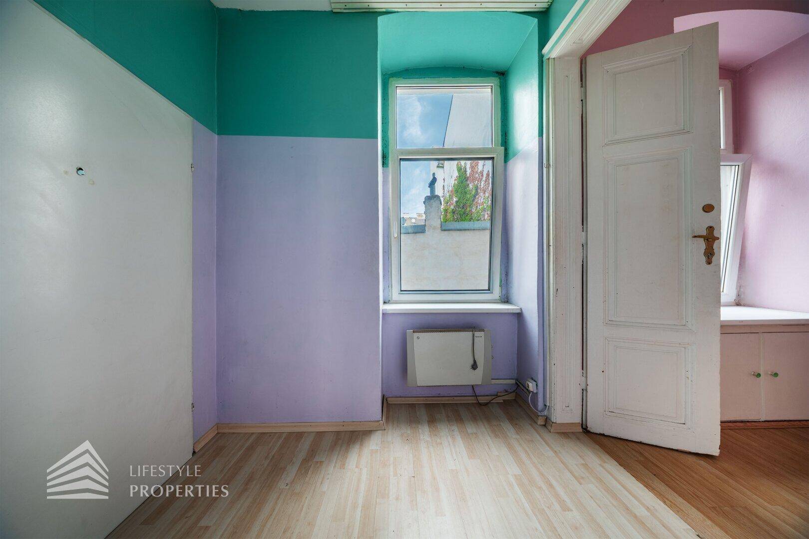 Helles Zimmer mit lila und türkisen Wänden, Holzboden und einem Fenster mit Blick nach draußen.