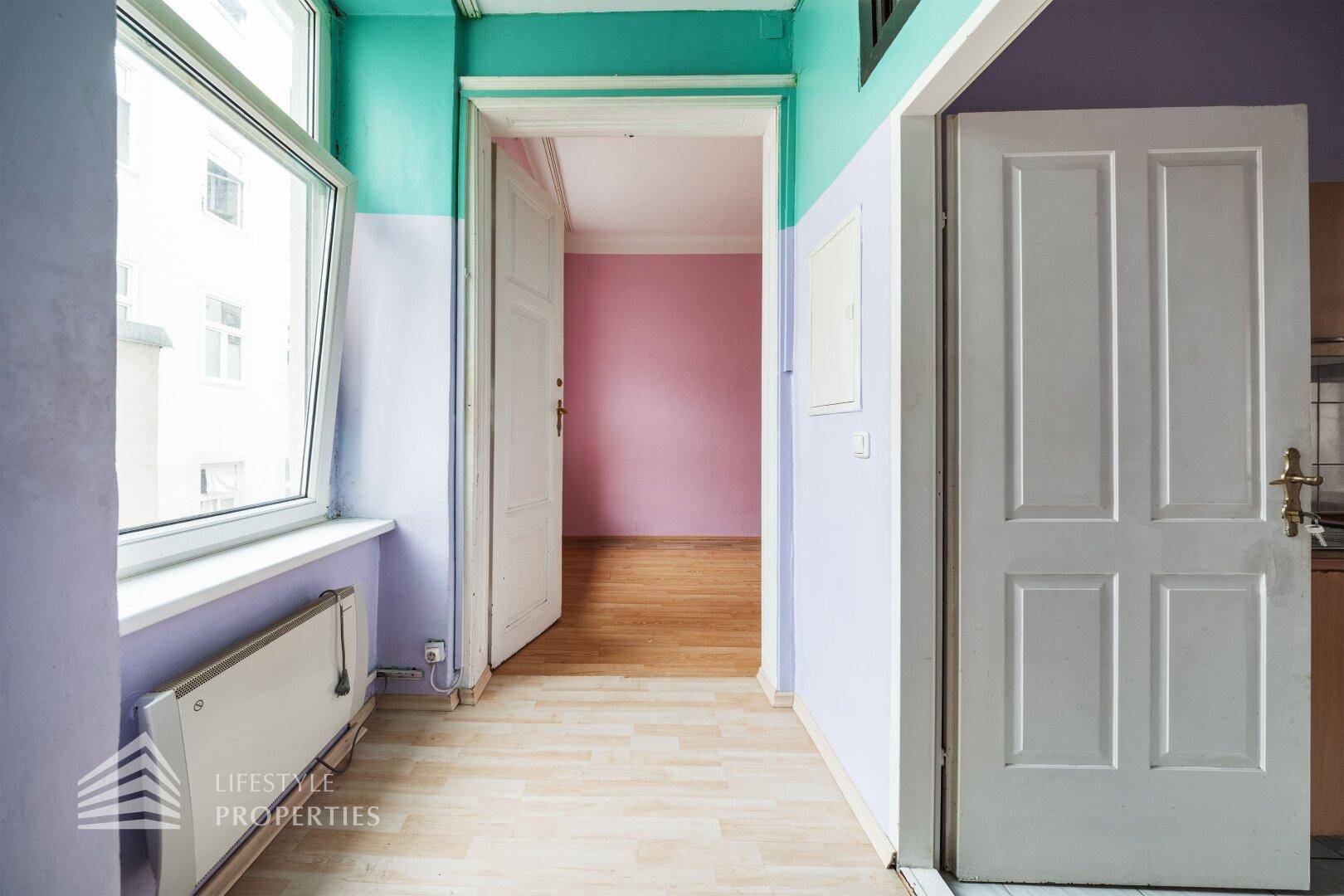 Flur mit lila und türkisen Wänden, Holzboden und einer offenen Tür zu einem weiteren Zimmer.