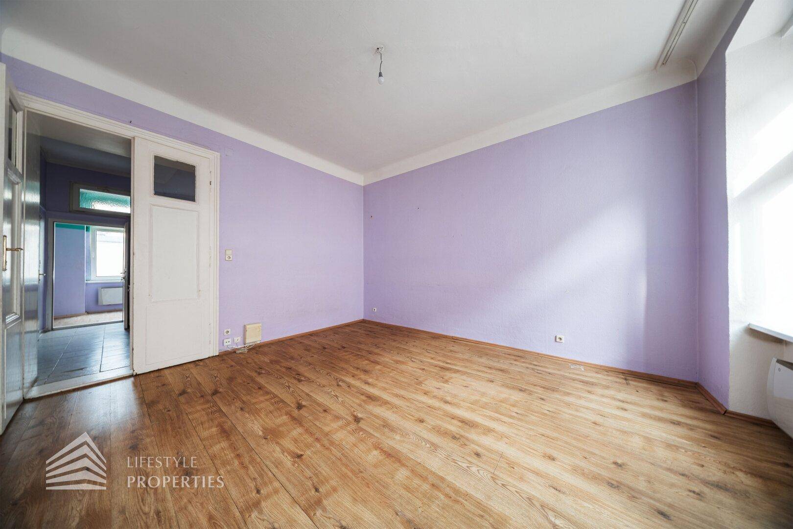Geräumiges Zimmer mit lila Wänden, Holzboden und einer Schiebetür zu einem angrenzenden Raum.