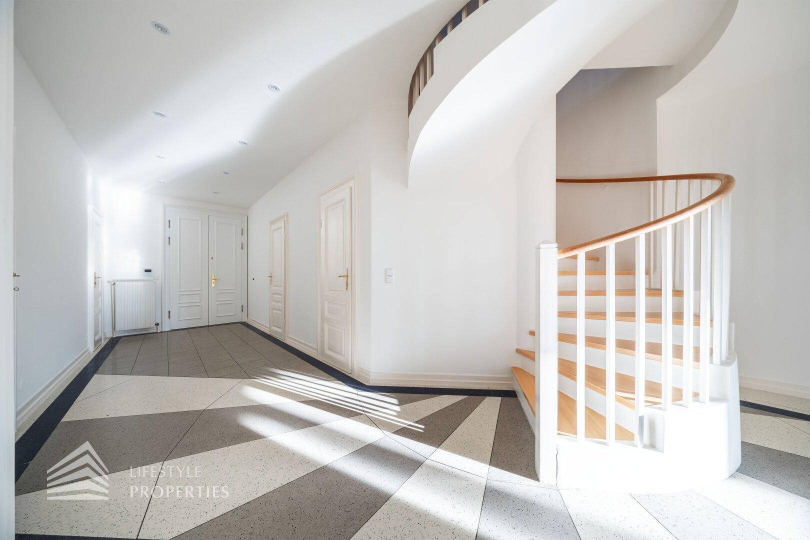 Eleganter Flur mit gemustertem Fliesenboden und geschwungener Holztreppe.