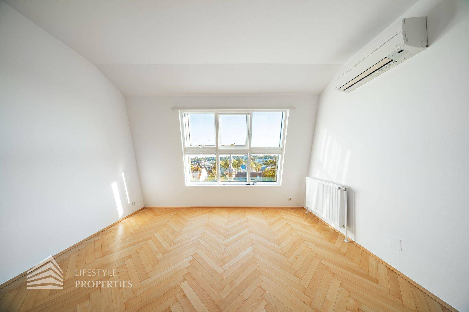 Helles Schlafzimmer im Dachgeschoss mit Fischgrätparkett und großem Fenster mit Ausblick.