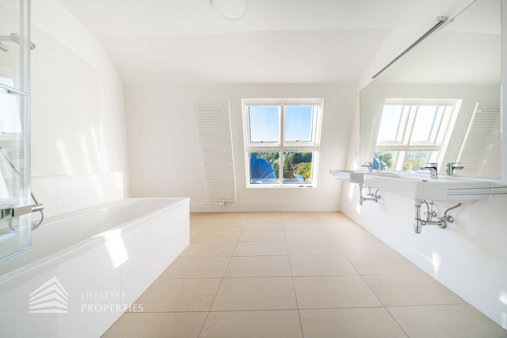 Helles Badezimmer mit Badewanne, Doppelwaschbecken und großem Fenster mit Ausblick.