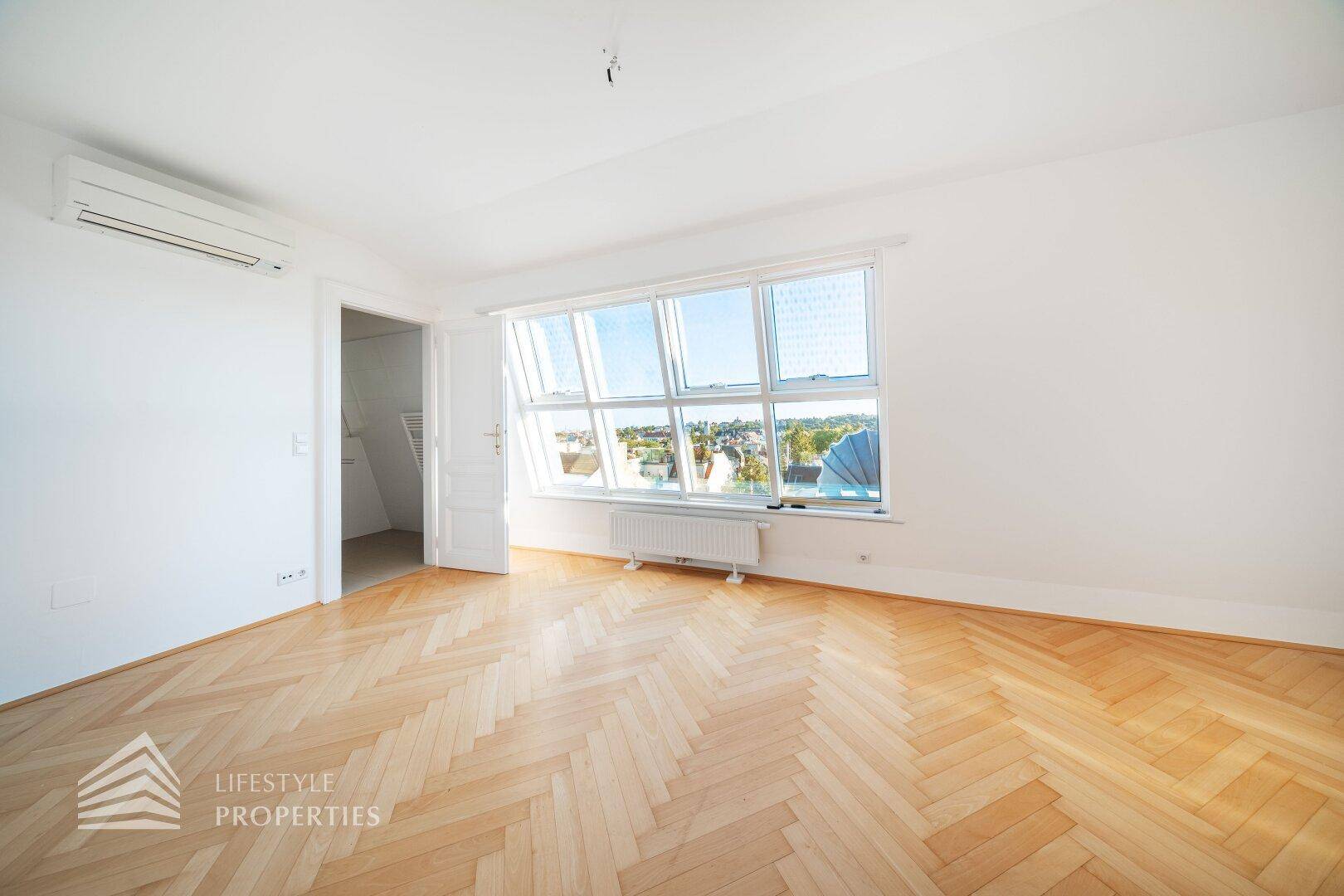 Helles Zimmer mit Fischgrätparkett, großen Dachfenstern und Klimaanlage, ideal als Schlafzimmer.