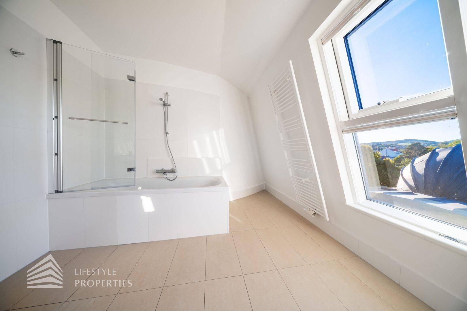 Modernes Badezimmer mit Badewanne, Duschabtrennung und großem Fenster, das viel Licht hereinlässt.