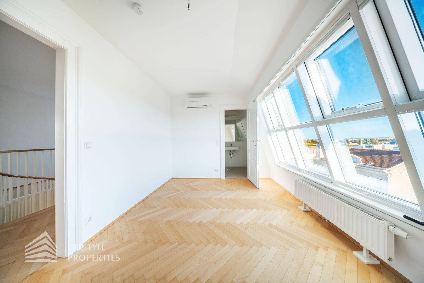 Geräumiges Zimmer mit Fischgrätparkett, großen Fenstern und Zugang zu einem weiteren Raum.