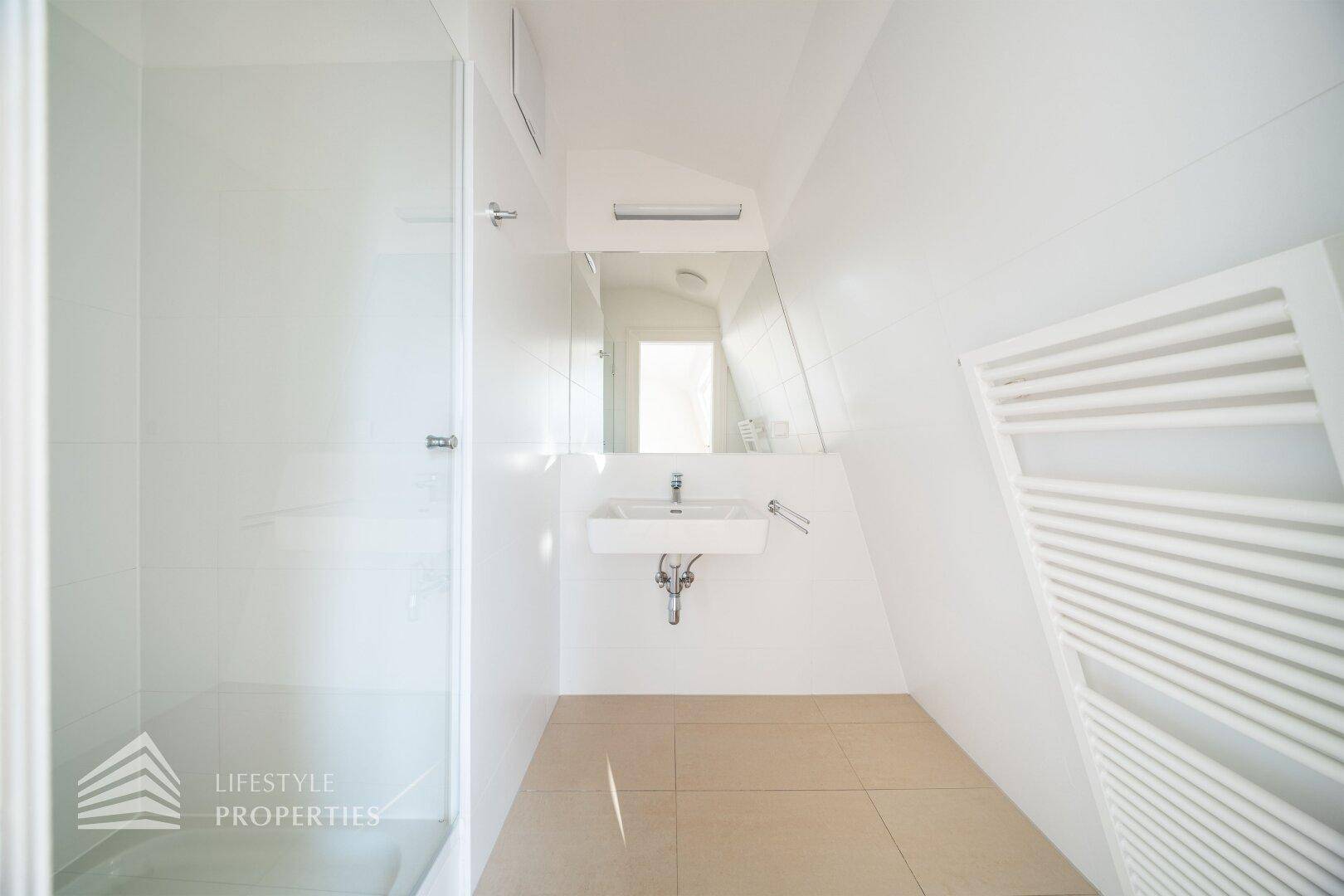 Modernes Badezimmer mit Dusche, Einzelwaschbecken und beheiztem Handtuchhalter in heller Ausführung.