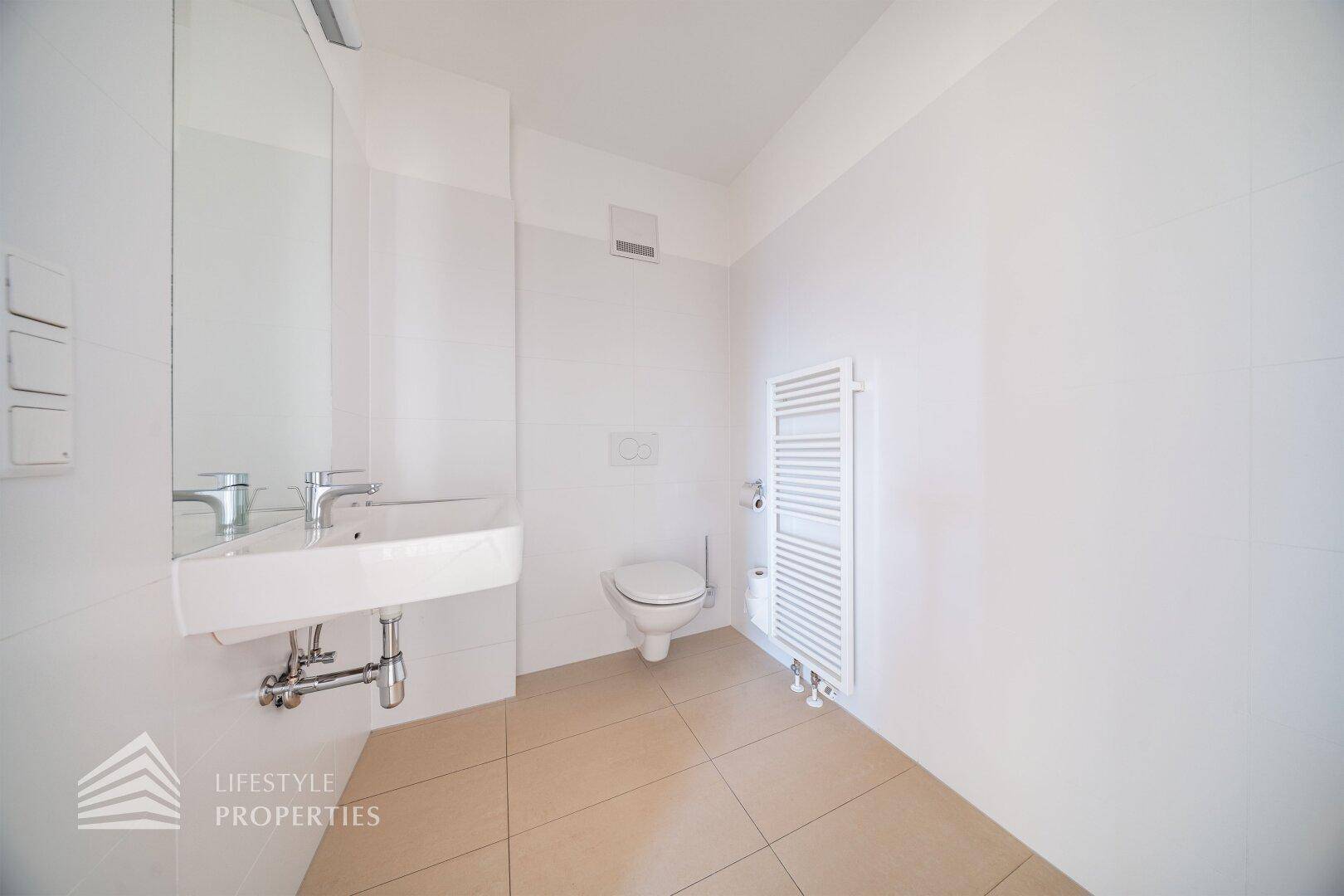 Helles Gäste-WC mit wandhängender Toilette, Einzelwaschbecken und beheiztem Handtuchhalter.