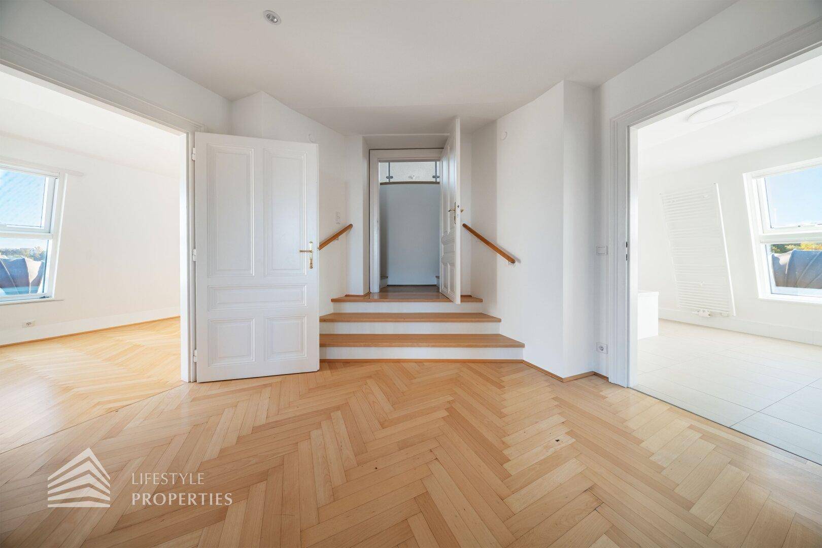 Heller Flurbereich mit Fischgrätparkett und Zugang zu mehreren Zimmern, inklusive Treppe.