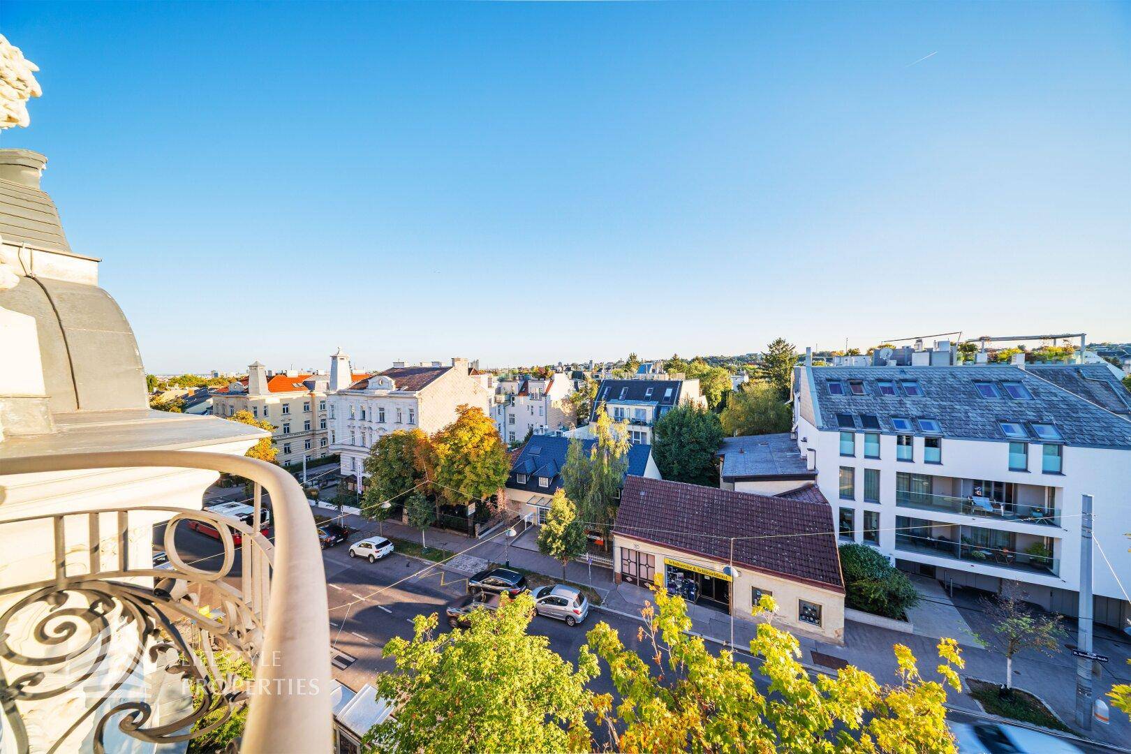 Balkon mit Blick auf die umliegende Stadtbebauung und grüne Bäume unter blauem Himmel.