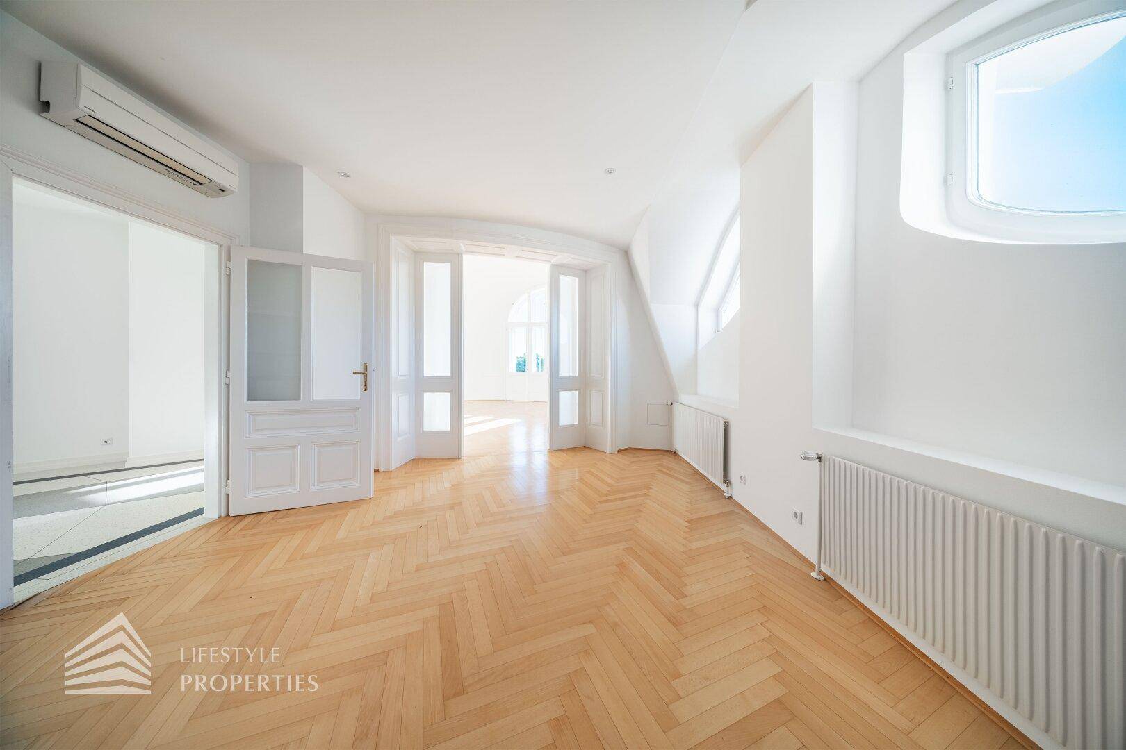 Heller Raum mit Fischgrätparkett, Heizkörpern und Zugang zu anderen Bereichen der Wohnung.
