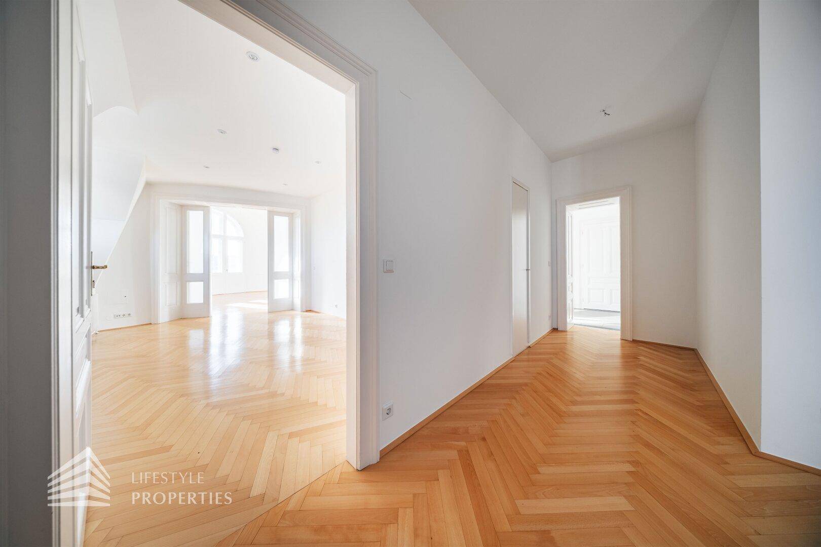 Heller Flur mit Fischgrätparkett, der zu verschiedenen Räumen der Wohnung führt.