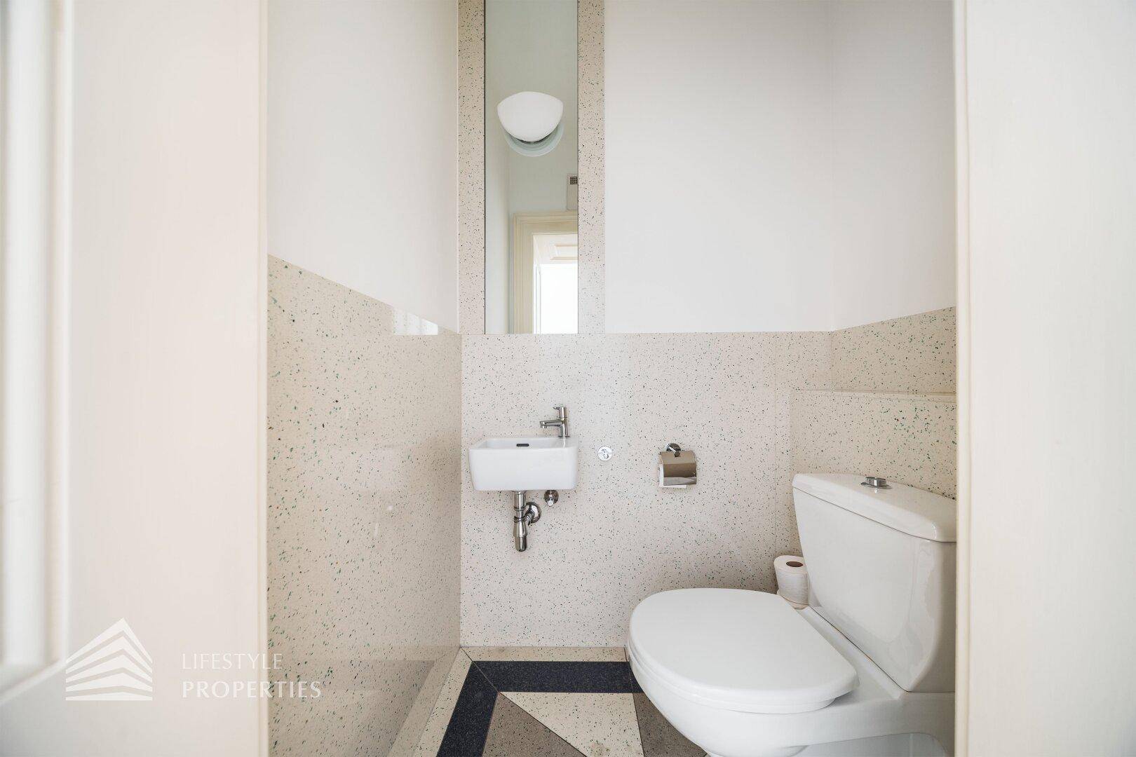 Kleines Gäste-WC mit Toilette, Waschbecken und dekorativen Fliesen an den Wänden.