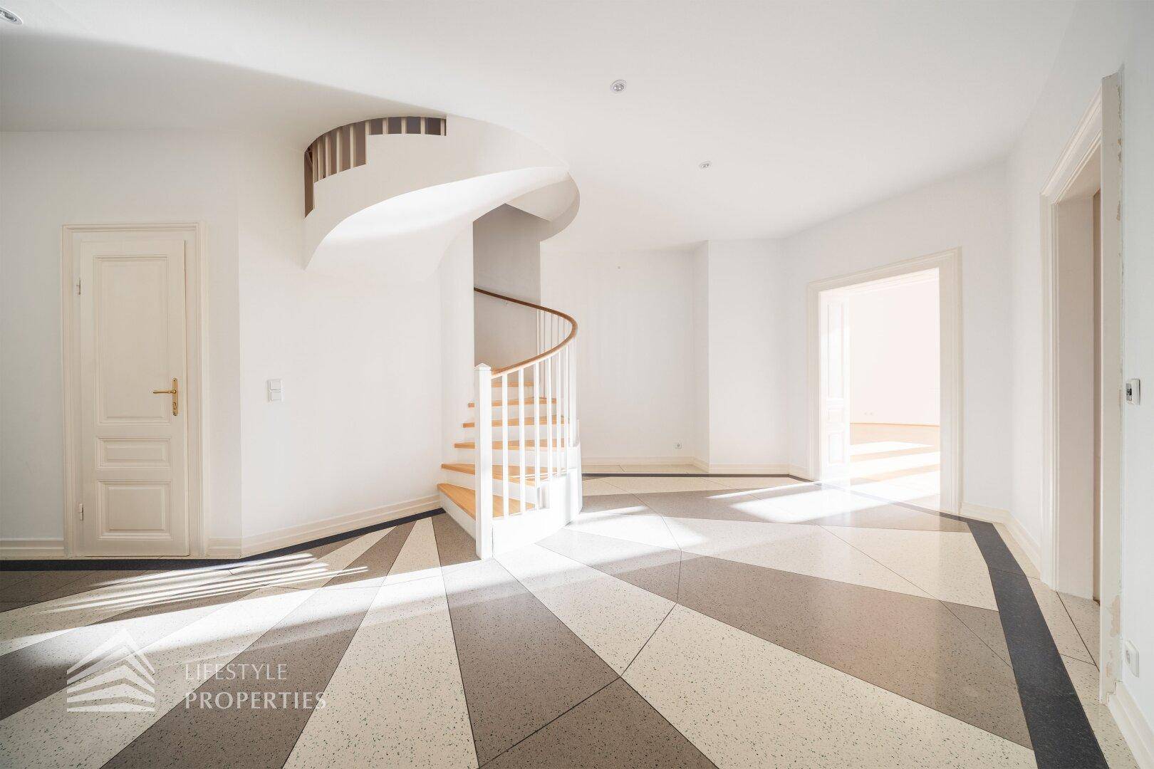 Heller Eingangsbereich mit auffälligem Fliesenboden und eleganter Wendeltreppe, lichtdurchflutet.