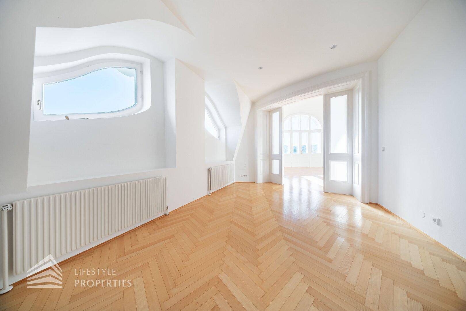 Helles Dachgeschosszimmer mit Fischgrätparkett und einem einzigartig geformten Fenster.