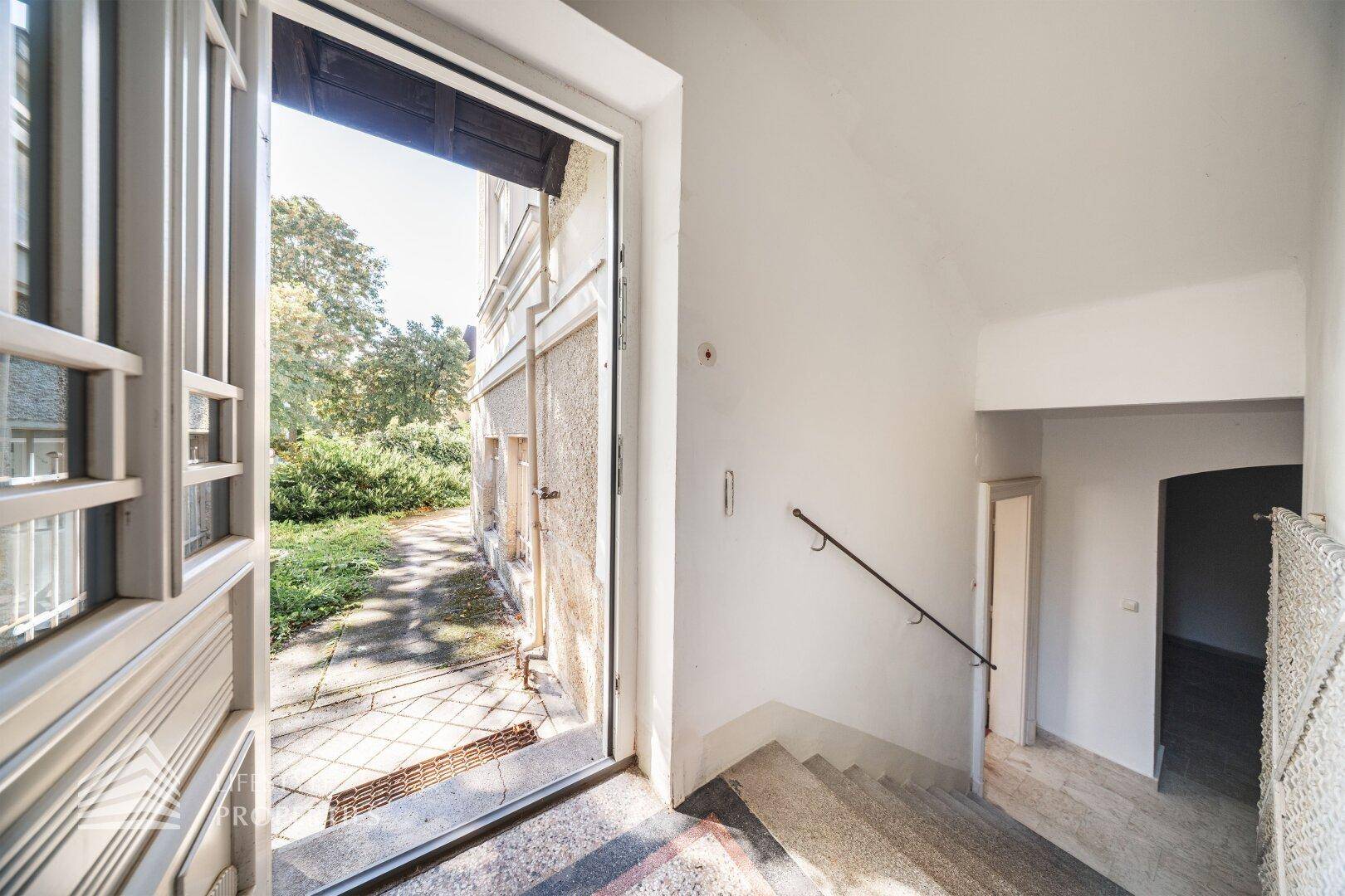 Eingangsbereich mit offener Tür, Treppe und Blick in den Garten.