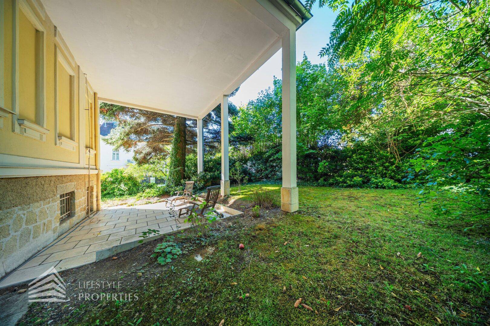 Geräumige überdachte Terrasse mit Steinplatten und angrenzendem Rasenbereich im Grünen.