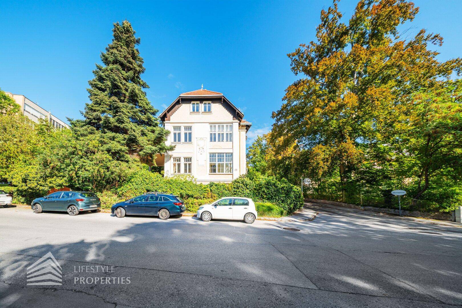 Frontansicht der charmanten Villa mit gepflegtem Vorgarten und parkenden Autos auf der Straße.