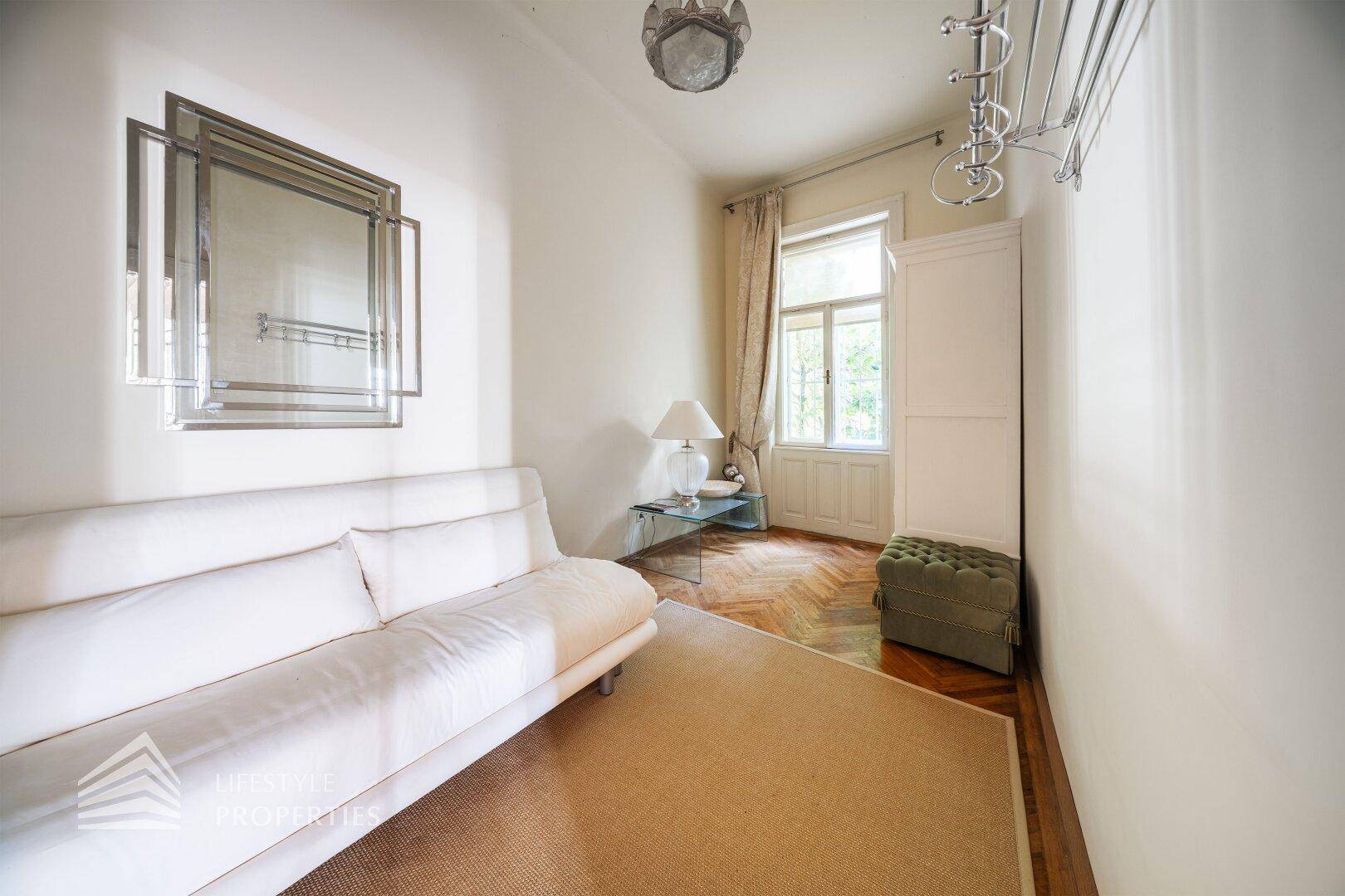 Gemütliches Schlafzimmer mit Parkettboden, weißem Sofa und Fenster mit Blick ins Grüne.