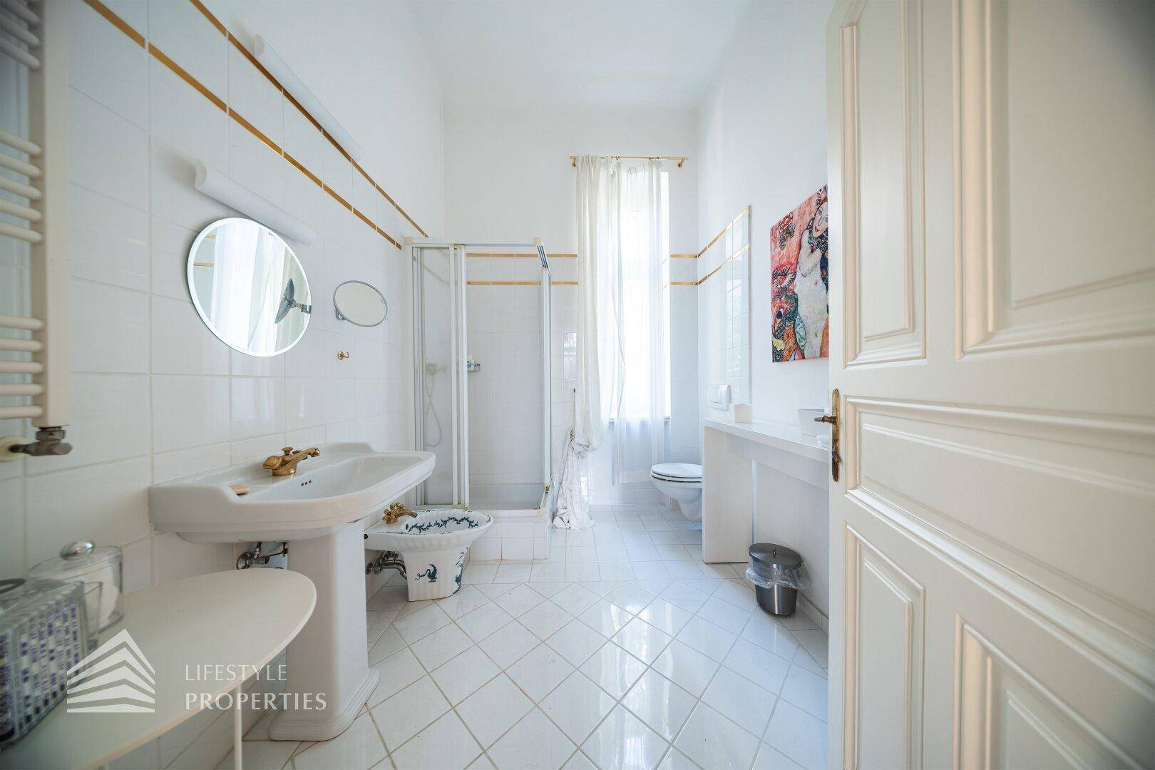 Helles Badezimmer mit weißen Fliesen, Dusche, Standwaschbecken und Fenster.