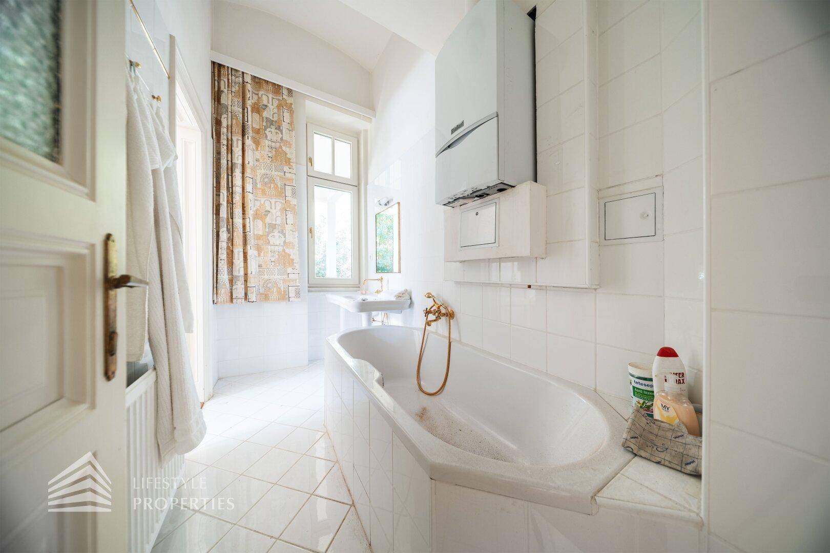 Badezimmer mit Badewanne, weißen Fliesen und Fenster, ausgestattet mit Gastherme.