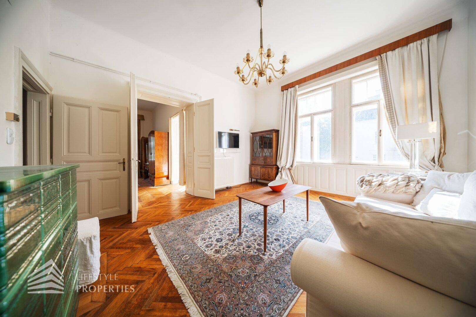 Helles Wohnzimmer mit Parkettboden, Kachelofen und Zugang zu weiteren Räumen der Villa.
