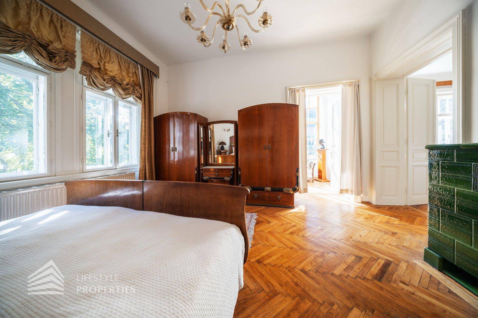 Helles Schlafzimmer mit Parkettboden, antiken Möbeln und großen Fenstern mit viel Licht.