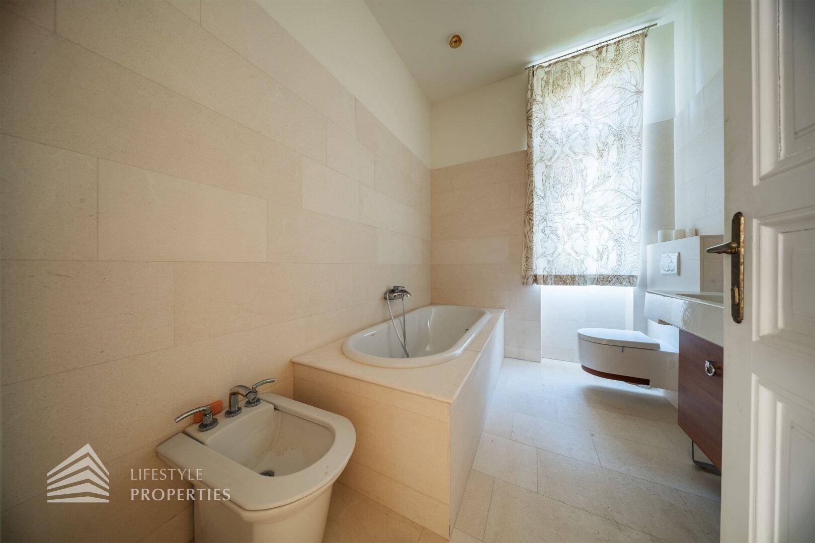 Helles Badezimmer mit Badewanne, Bidet und beigefarbenen Fliesen.