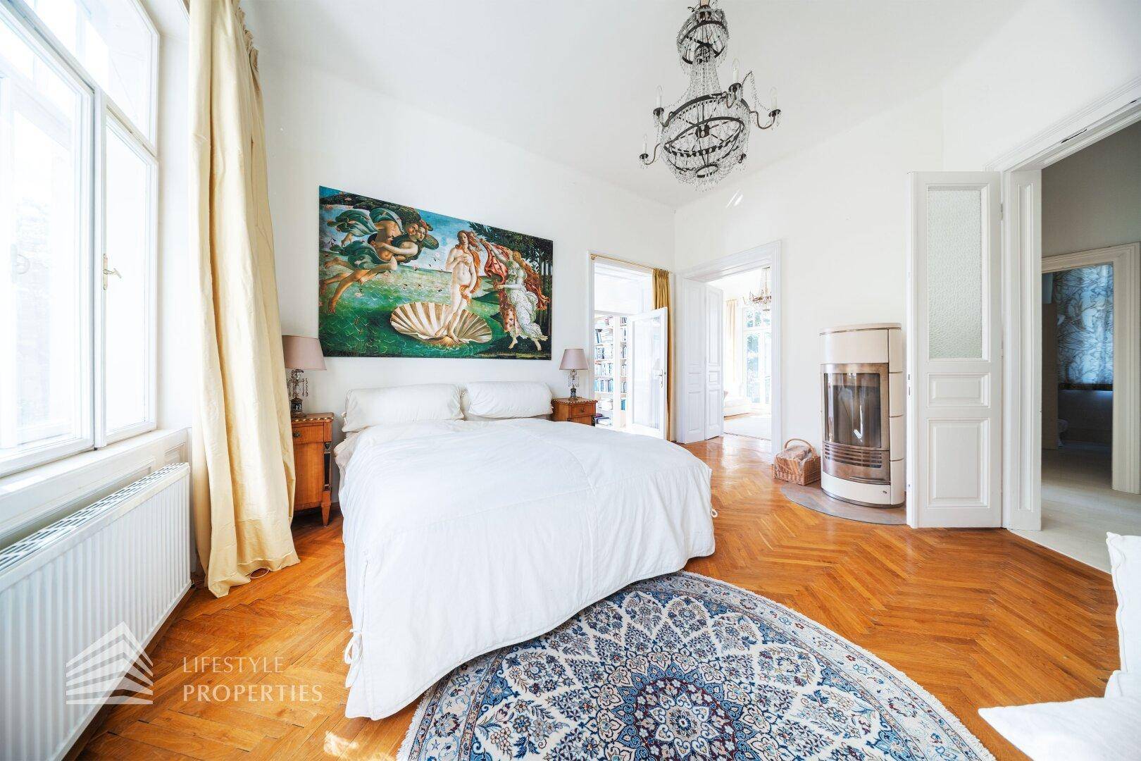 Helles Schlafzimmer mit Fischgrätparkett, Kaminofen und Kunstwerk an der Wand.