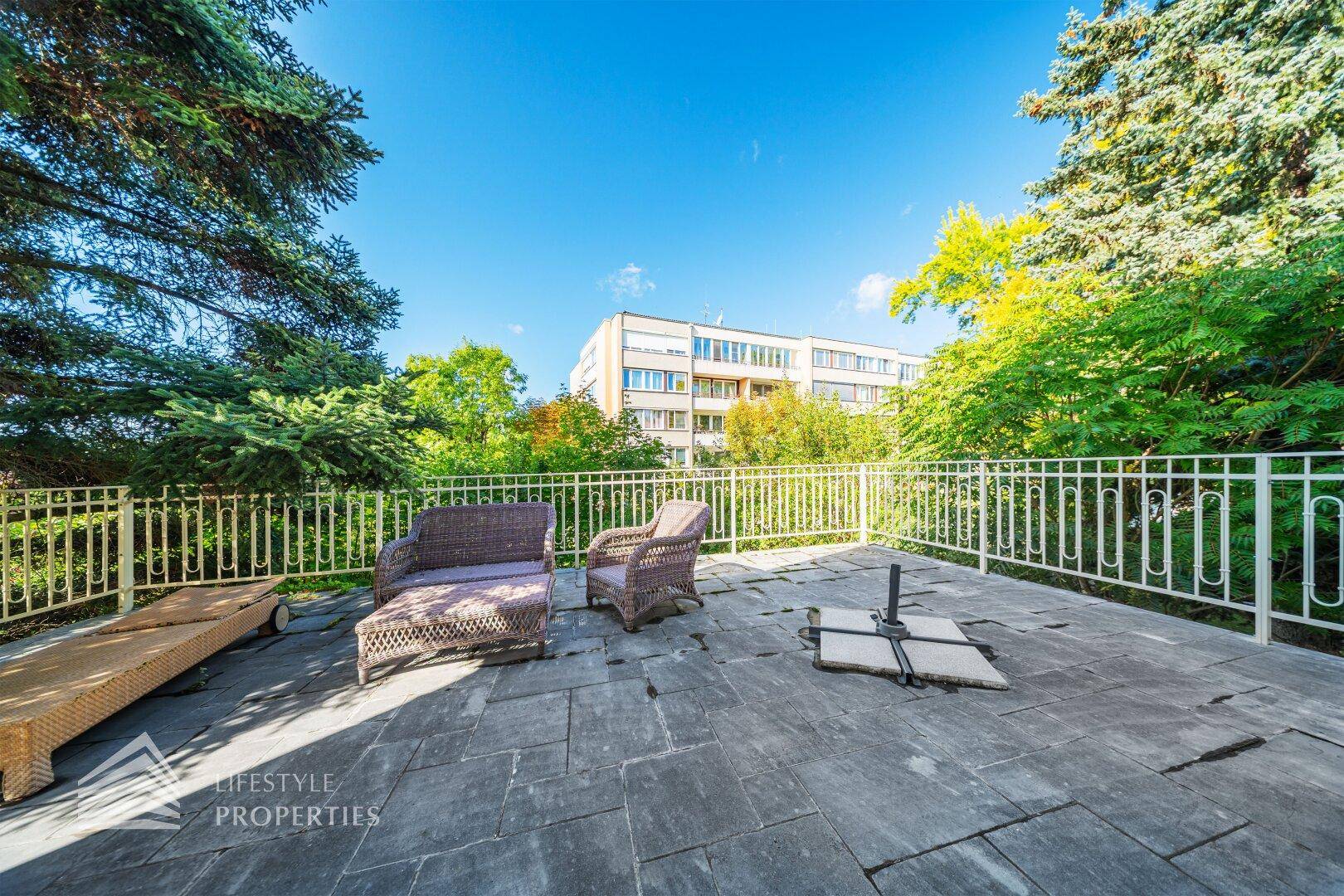 Große Steinterrasse mit Gartenmöbeln und Blick auf umliegende Gebäude und Bäume.