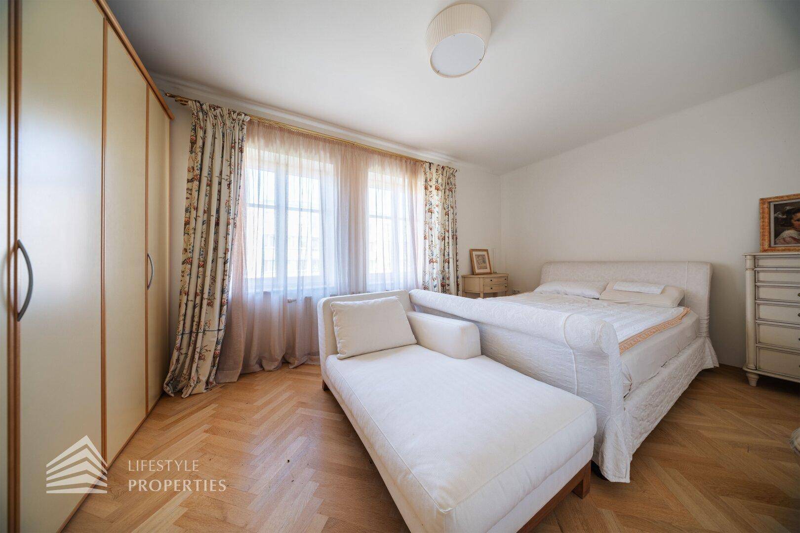 Helles Schlafzimmer mit Doppelbett, Chaiselongue und großem Kleiderschrank, Parkettboden.