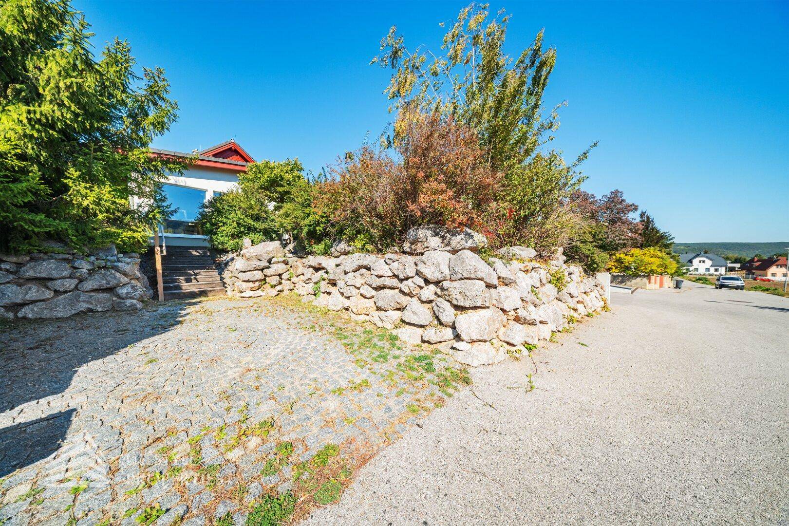 Gepflasterte Auffahrt mit Natursteinmauern, die zum Eingang des Hauses führt.