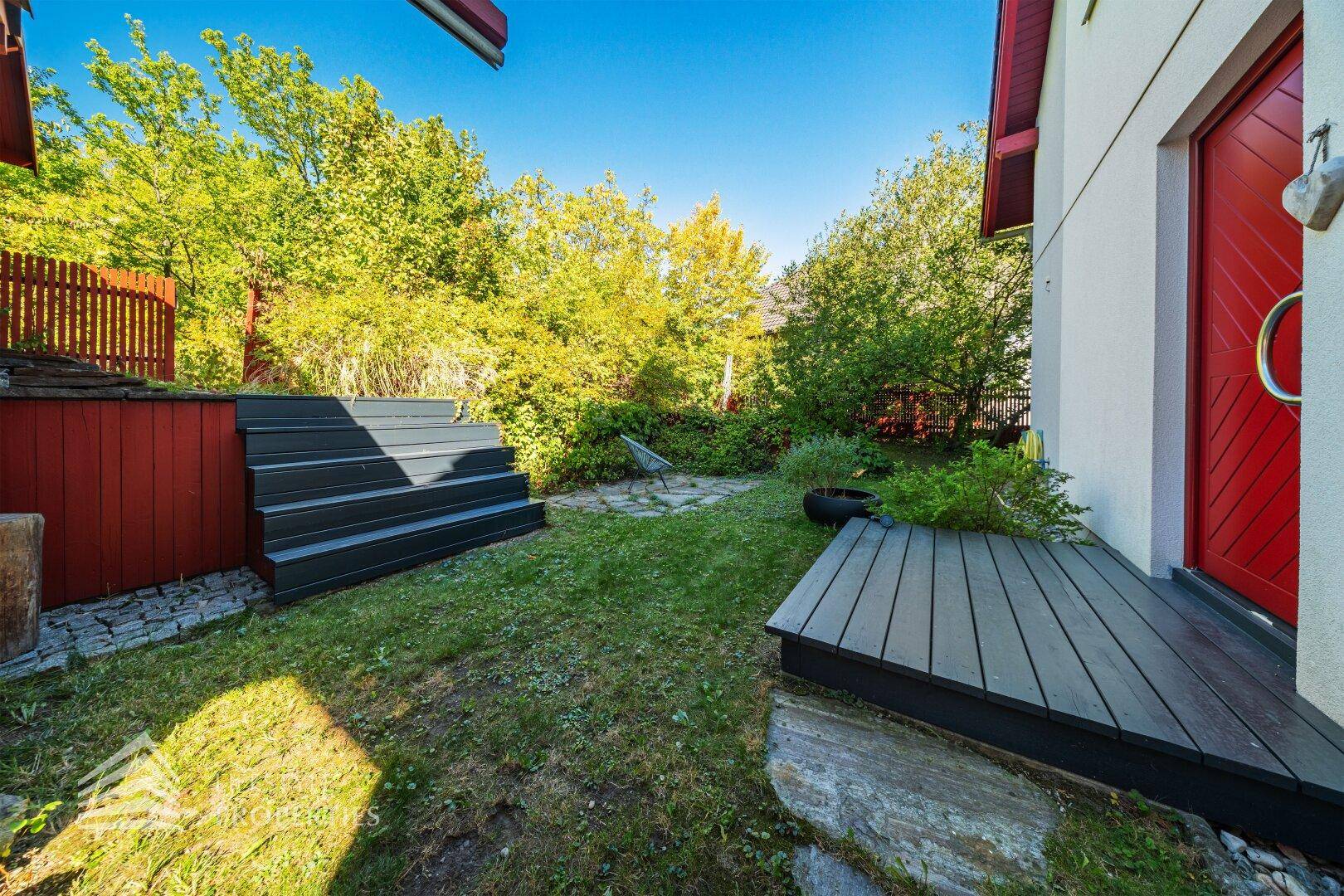 Kleiner Holzsteg neben dem Haus, der in den grünen Gartenbereich führt.