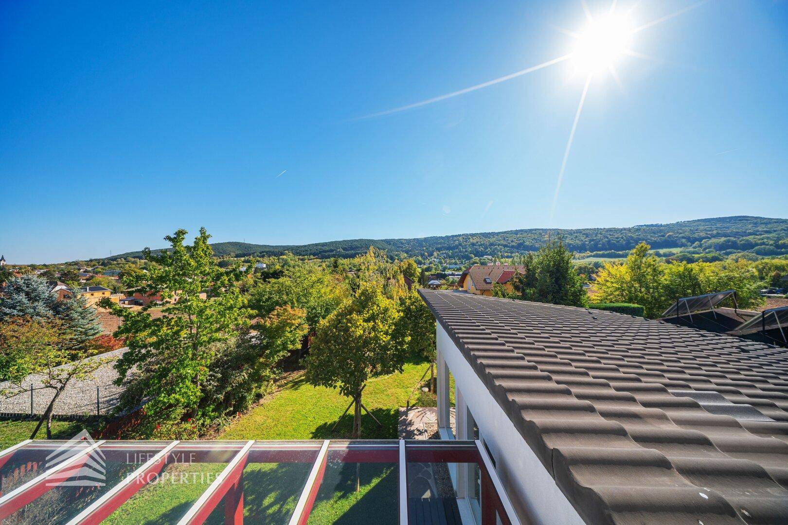 Panoramablick über das Hausdach und die umliegende grüne Landschaft unter strahlend blauem Himmel.