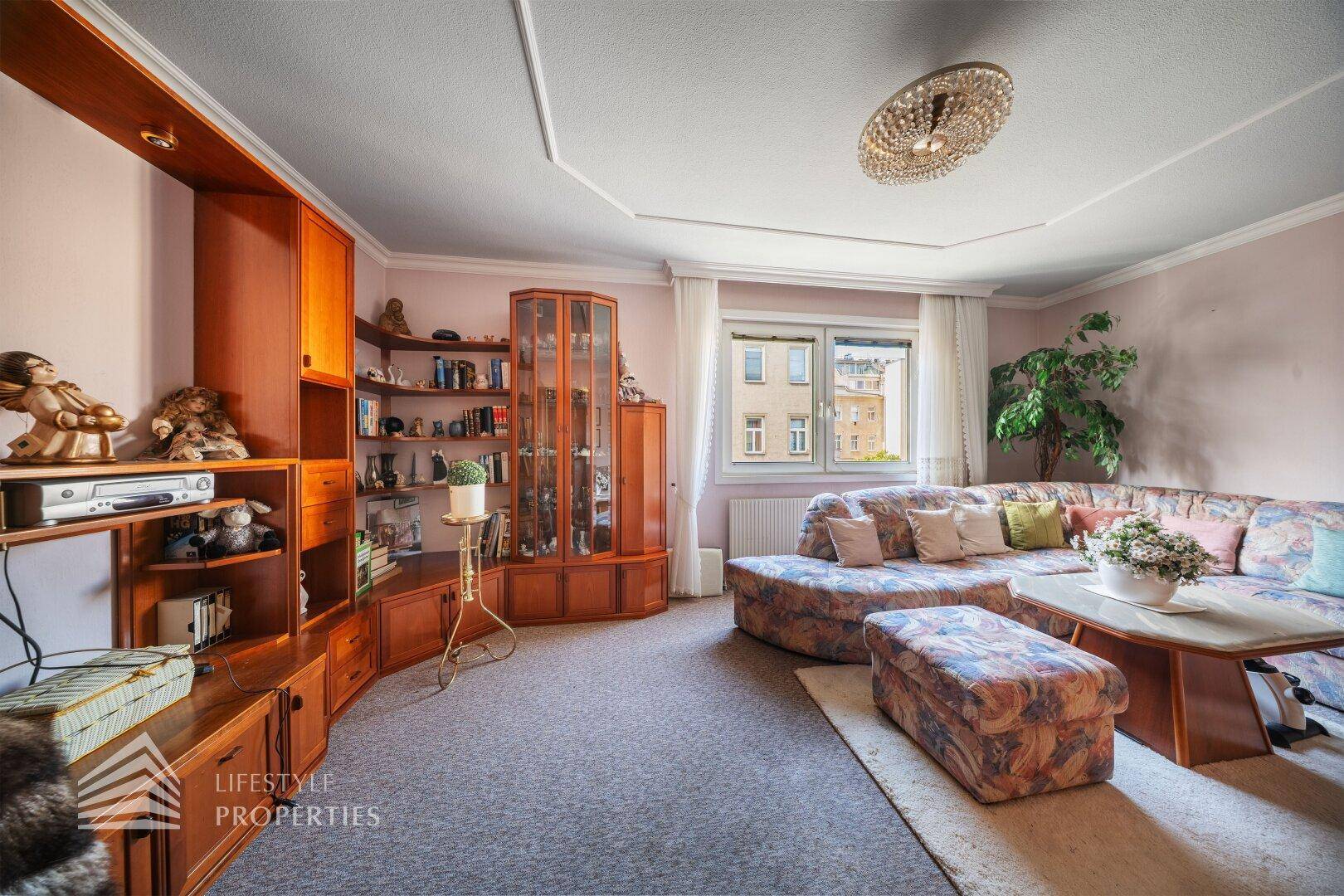 Geräumiges Wohnzimmer mit Ecksofa, Teppichboden und klassischer Deckenleuchte.