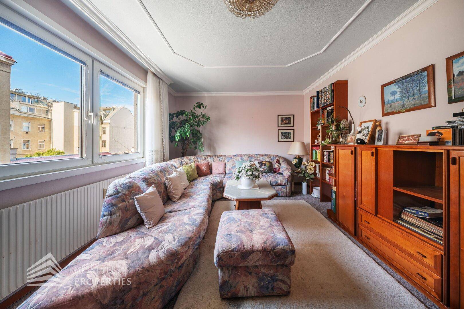 Helles Wohnzimmer mit bequemer Sitzecke, Teppichboden und Blick auf die umliegenden Gebäude.