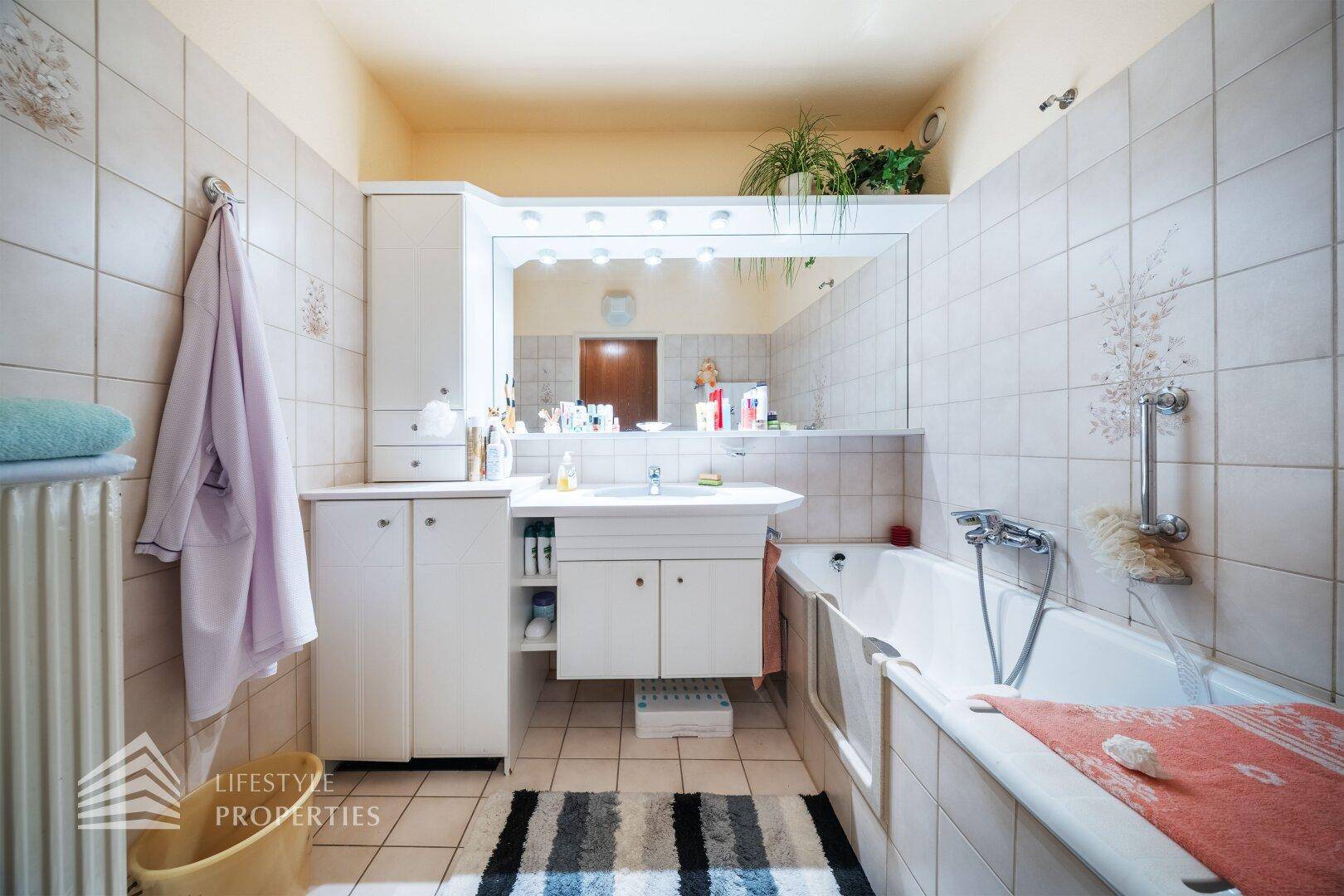 Gefliestes Badezimmer mit Badewanne, Waschbecken und großem Spiegel.