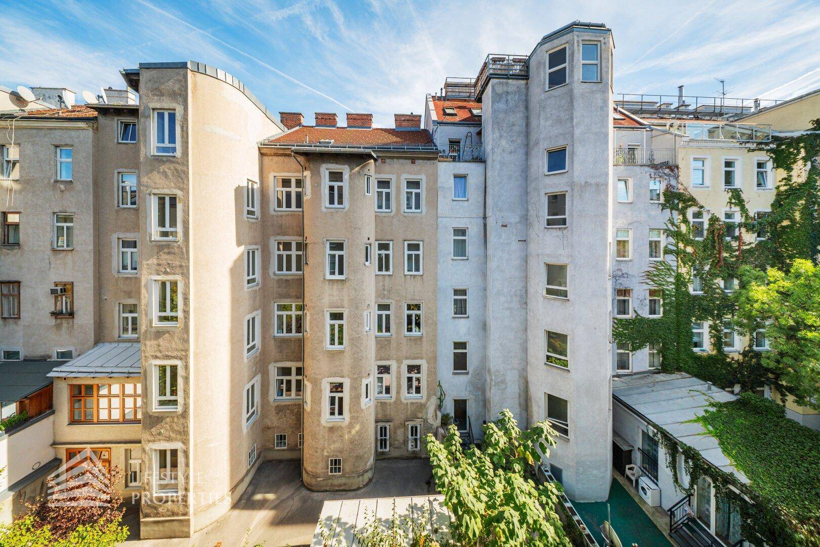 Innenhofansicht eines Mehrfamilienhauses mit vielen Fenstern und begrünten Fassaden.