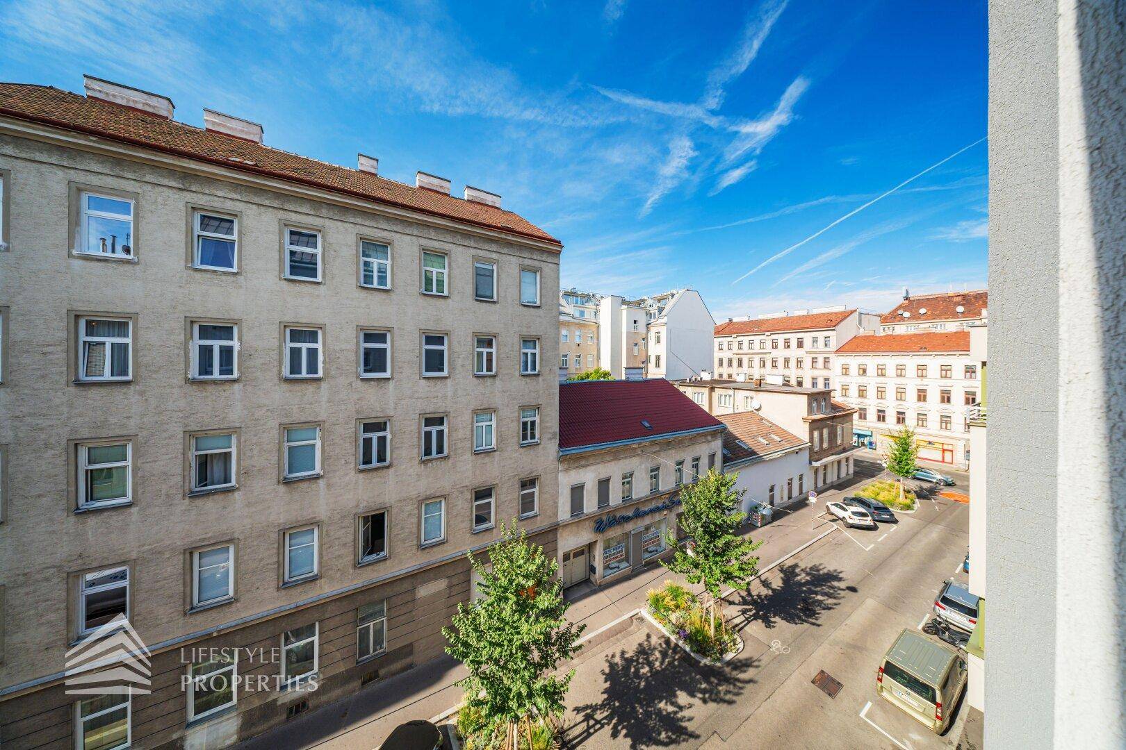 Straßenansicht eines Wohngebäudes mit parkenden Autos und blauem Himmel.