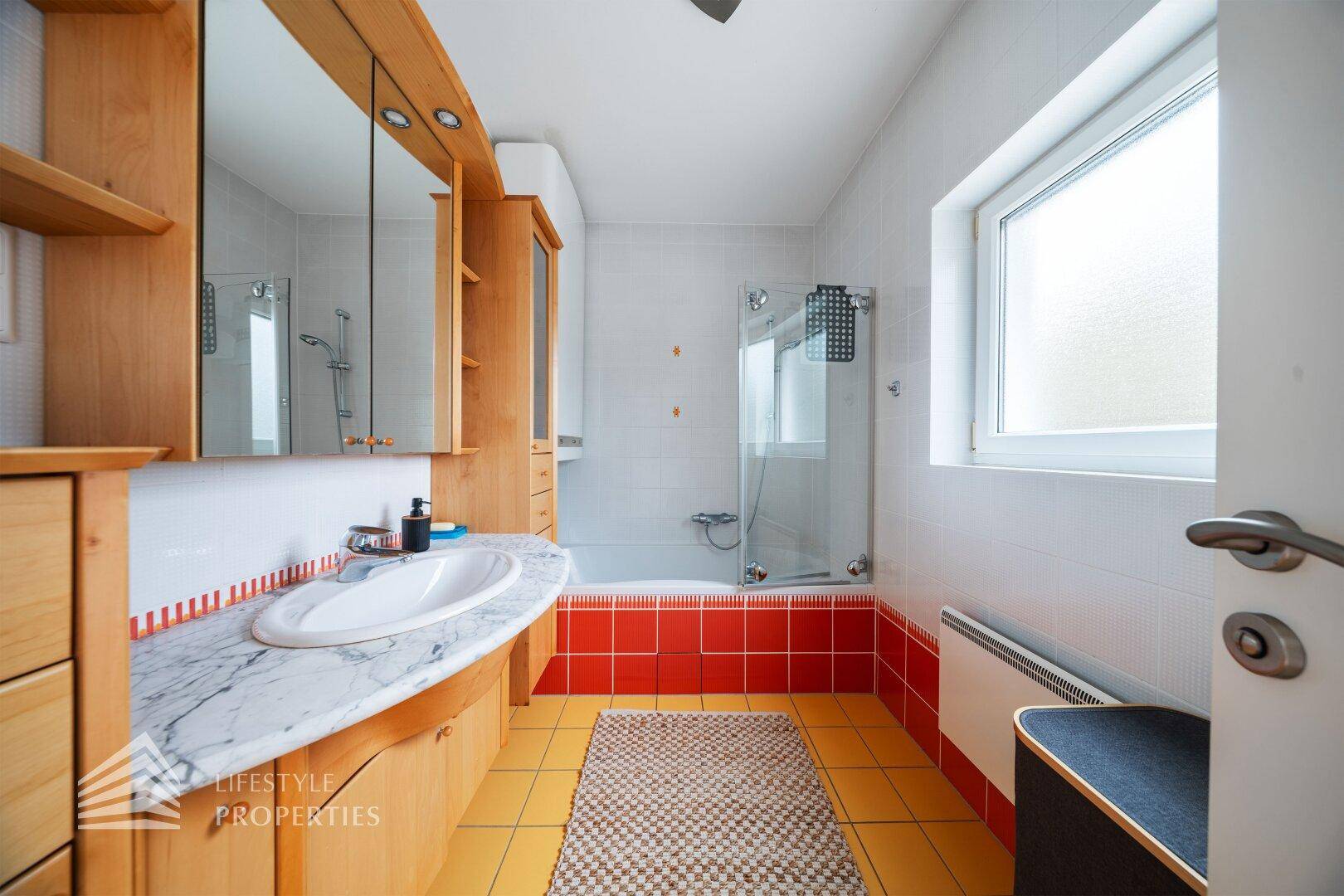 Badezimmer mit Badewanne, Marmorwaschtisch und Holzmöbeln in warmen Farbtönen.
