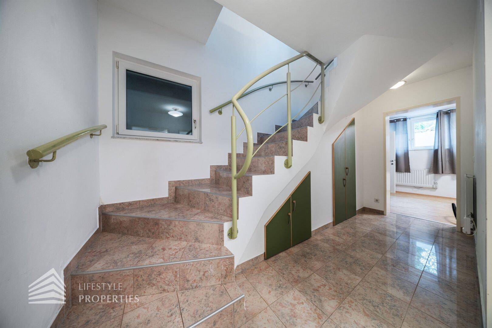 Treppenhaus mit gefliesten Stufen, Fenster und Stauraum unter der Treppe.