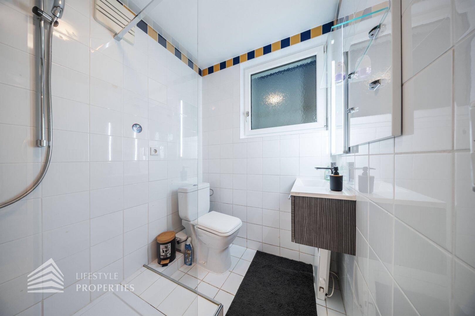 Badezimmer mit Dusche, WC, Waschbecken und weißen Fliesen.