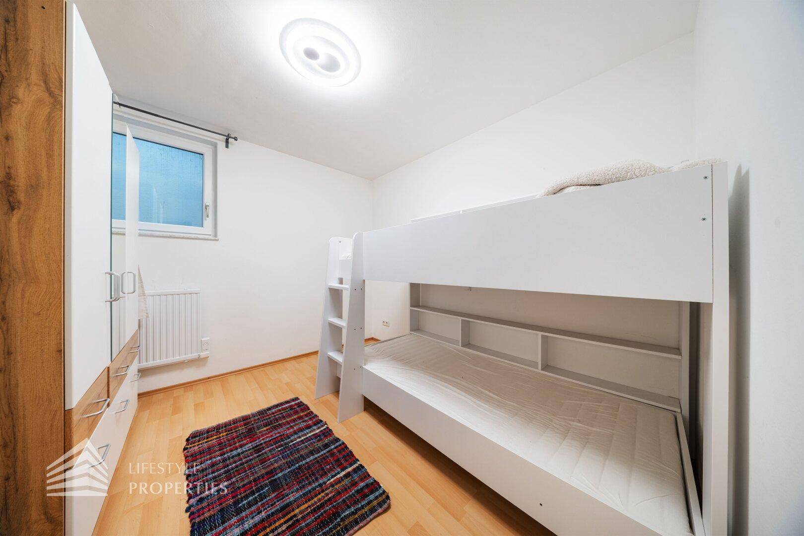Kinderzimmer mit Etagenbett, Holzfußboden und Fenster für natürliches Licht.