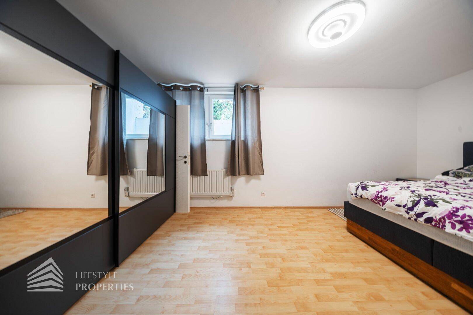 Schlafzimmer mit Doppelbett, Spiegelschrank und hellem Holzfußboden.