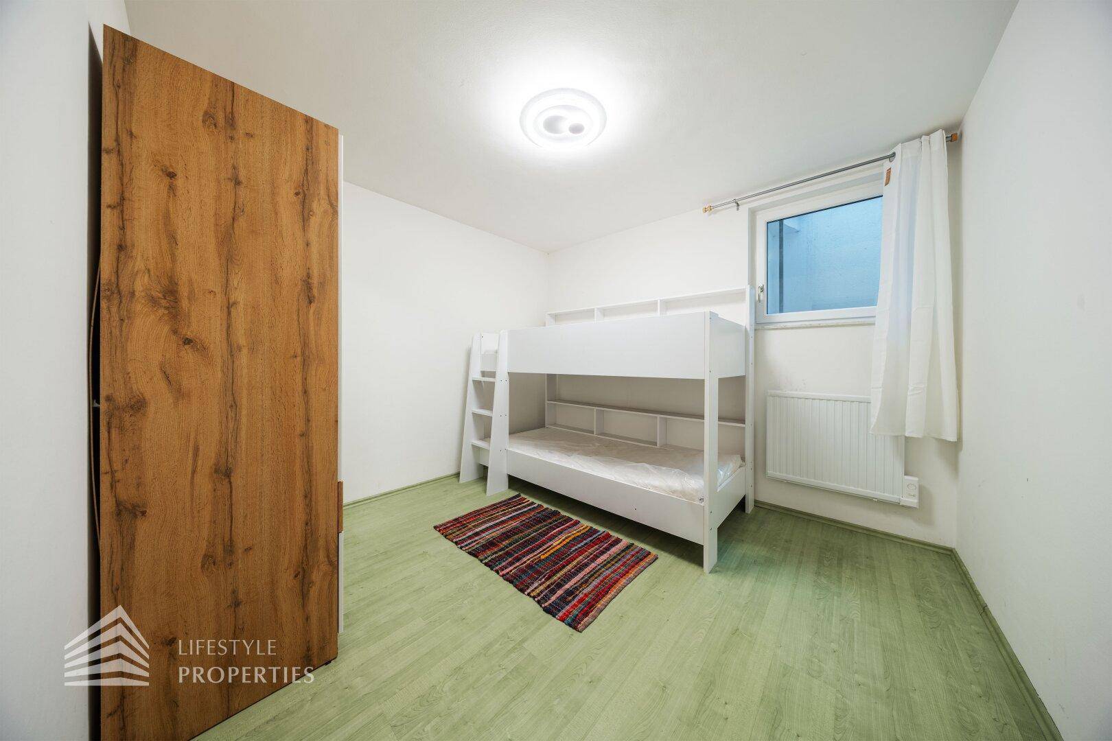 Schlafzimmer mit Etagenbett, Holzschrank und hellem Bodenbelag.